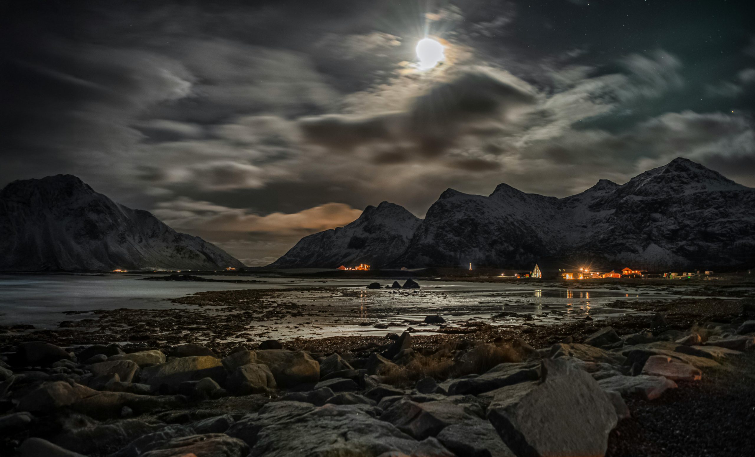 Paysage nocturne serein avec des montagnes et des nuages éclairés par la lune se reflétant sur l'eau.
