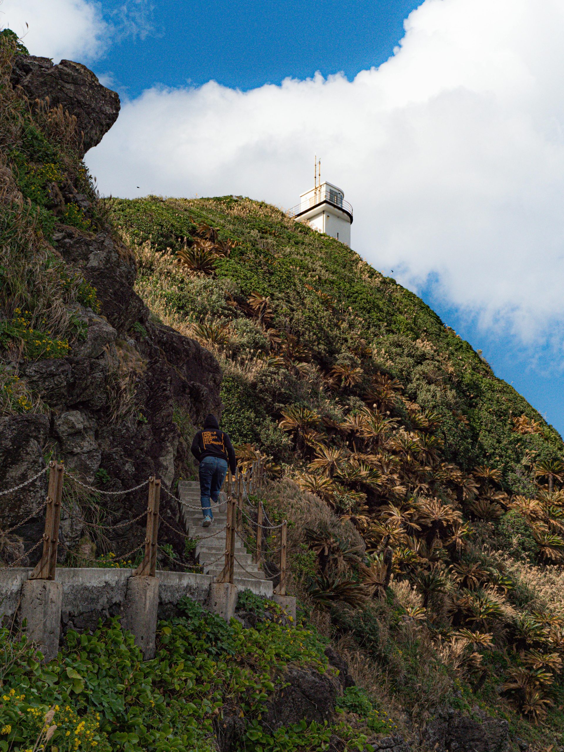 Une personne randonne sur un sentier pittoresque en direction d'un phare sur une colline verdoyante à Amami, au Japon.