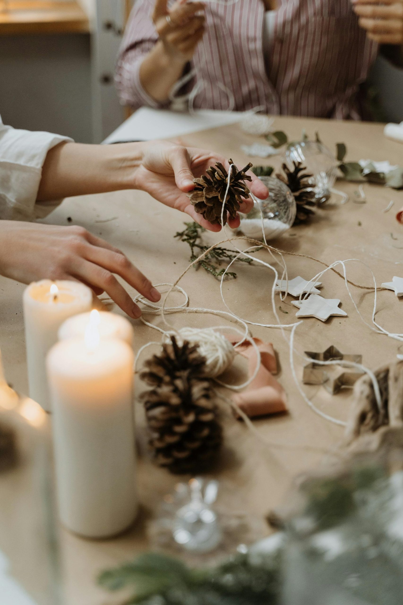 Mains créant de manière créative des décorations en pommes de pin sur une table chaleureuse avec des bougies, parfaites pour une touche artisanale.