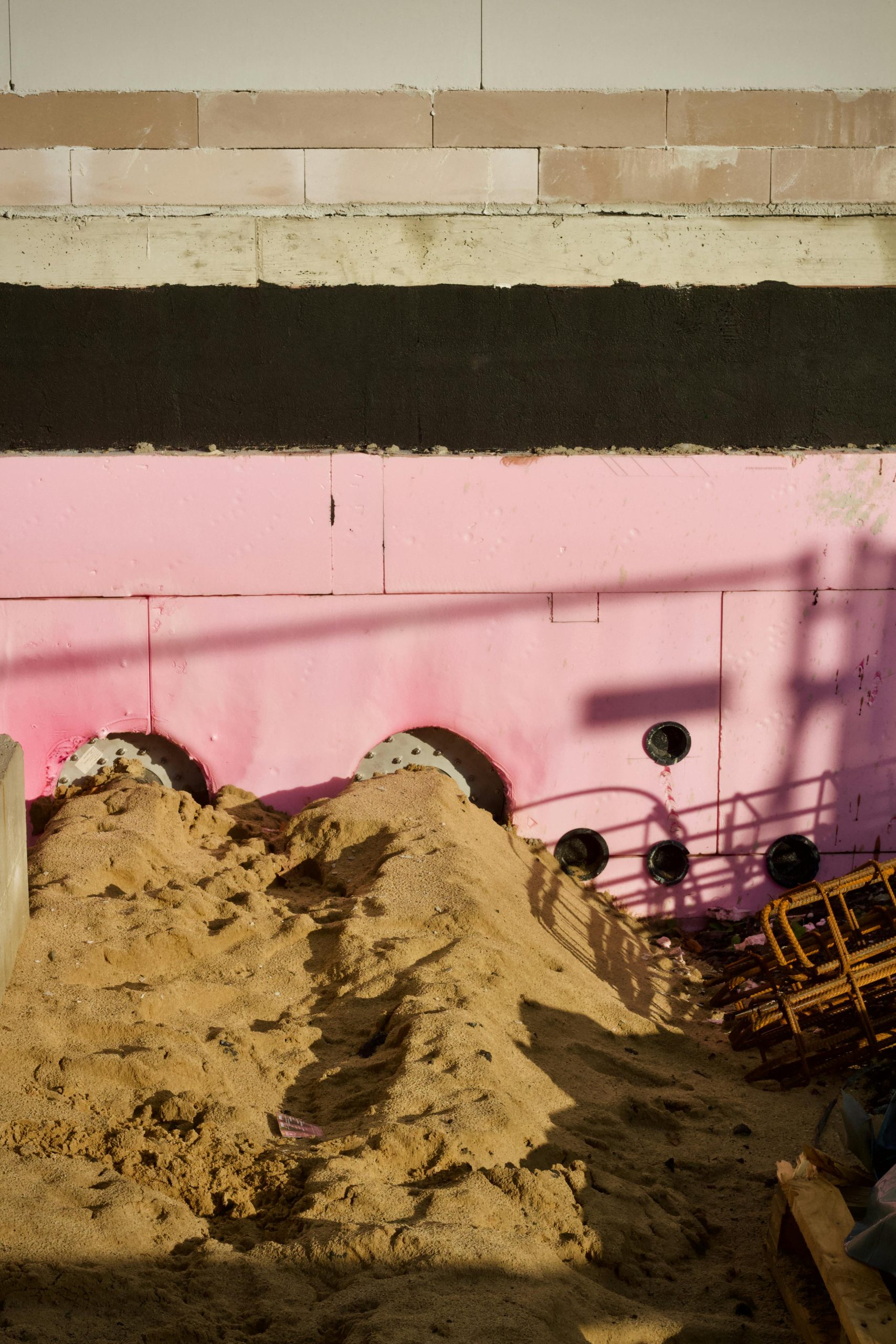 Image d'un chantier de construction mettant en avant des panneaux d'isolation roses sur un premier plan sableux.