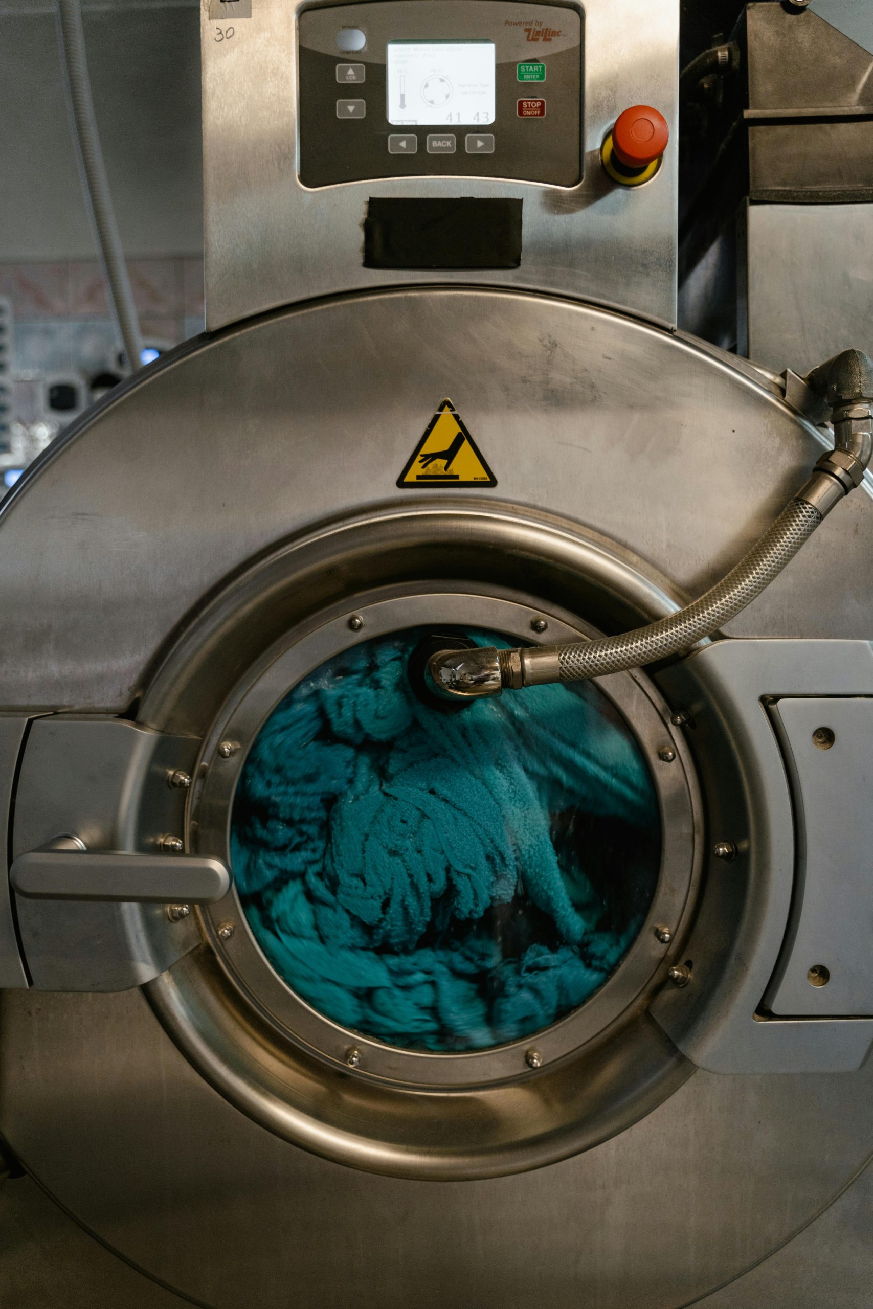 Close-up d'une machine à laver industrielle avec du tissu bleu pendant un cycle de lavage dans une laverie automatique.