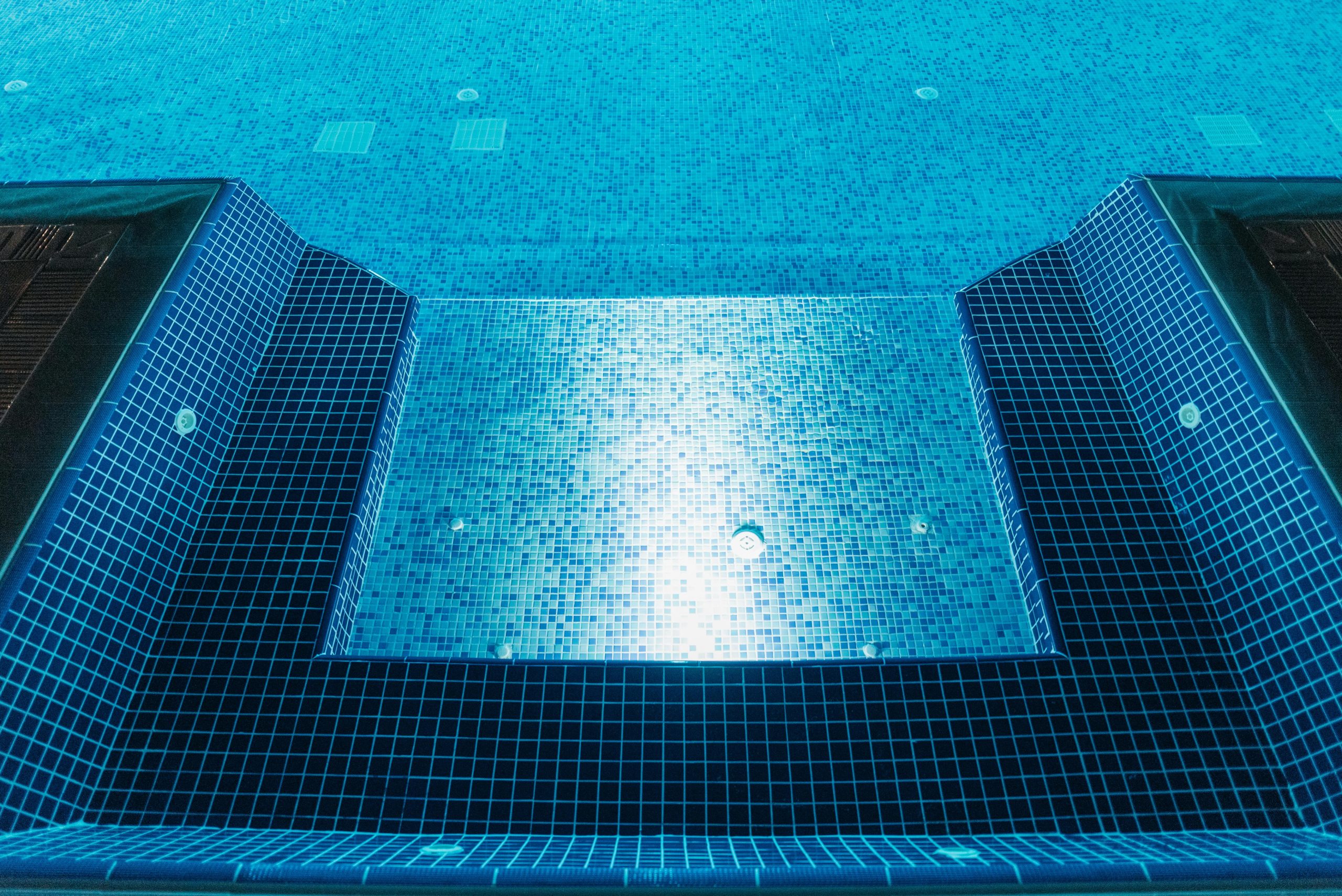 Une vue dégagée d'une piscine illuminée avec des carreaux de mosaïque bleus, parfaite pour la détente estivale.