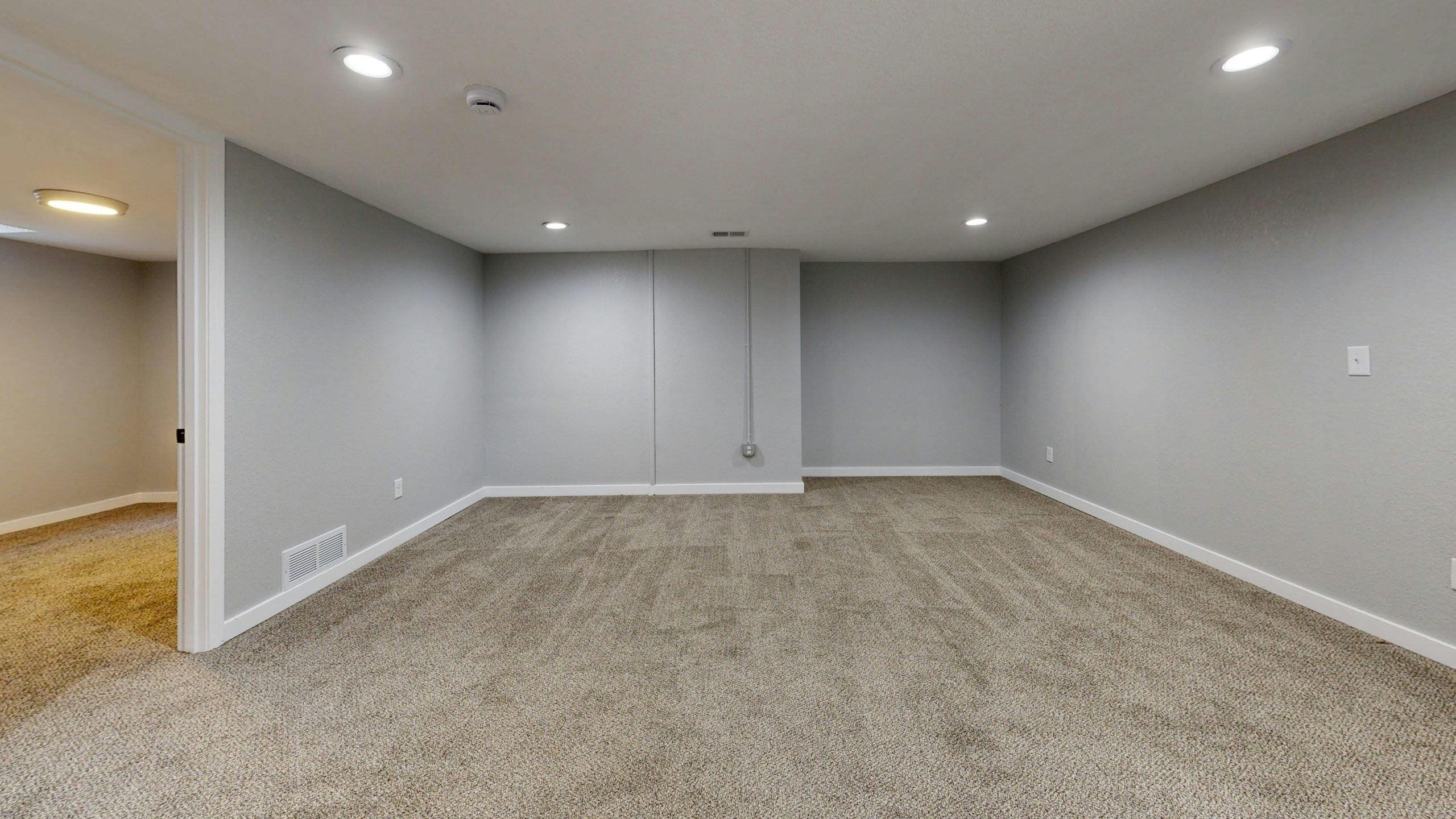 Open basement room with neutral gray walls and plush carpeting, ideal for remodeling. Pièce de sous-sol ouverte avec murs gris neutre et moquette moelleuse, idéale pour la rénovation.
