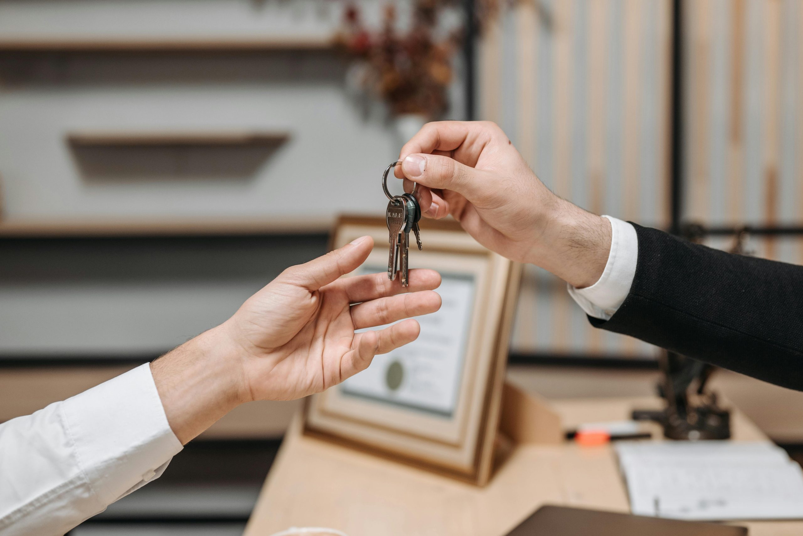 Detailed view of hands exchanging keys in a professional office environment, symbolizing real estate or business transactions. Vue détaillée des mains échangeant des clés dans un environnement de bureau professionnel, symbolisant des transactions immobilières ou commerciales.