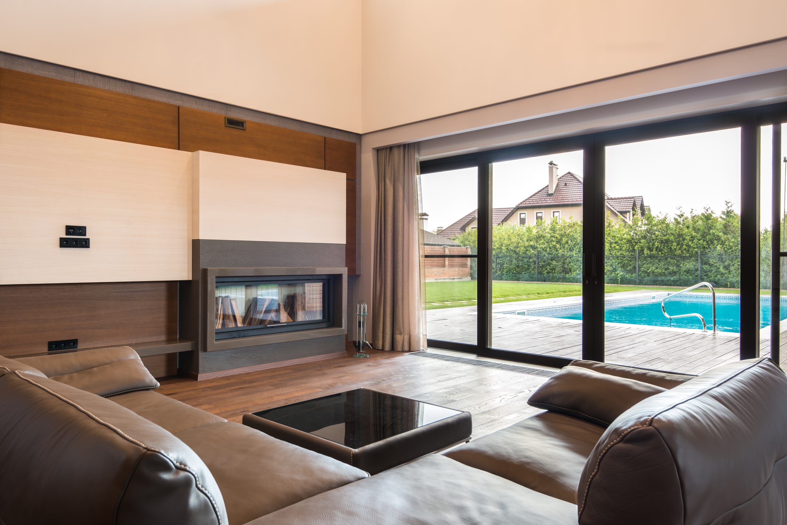Spacious modern living room with glass doors opening to a poolside area. Salon moderne spacieux avec portes vitrées donnant sur une zone de piscine.
