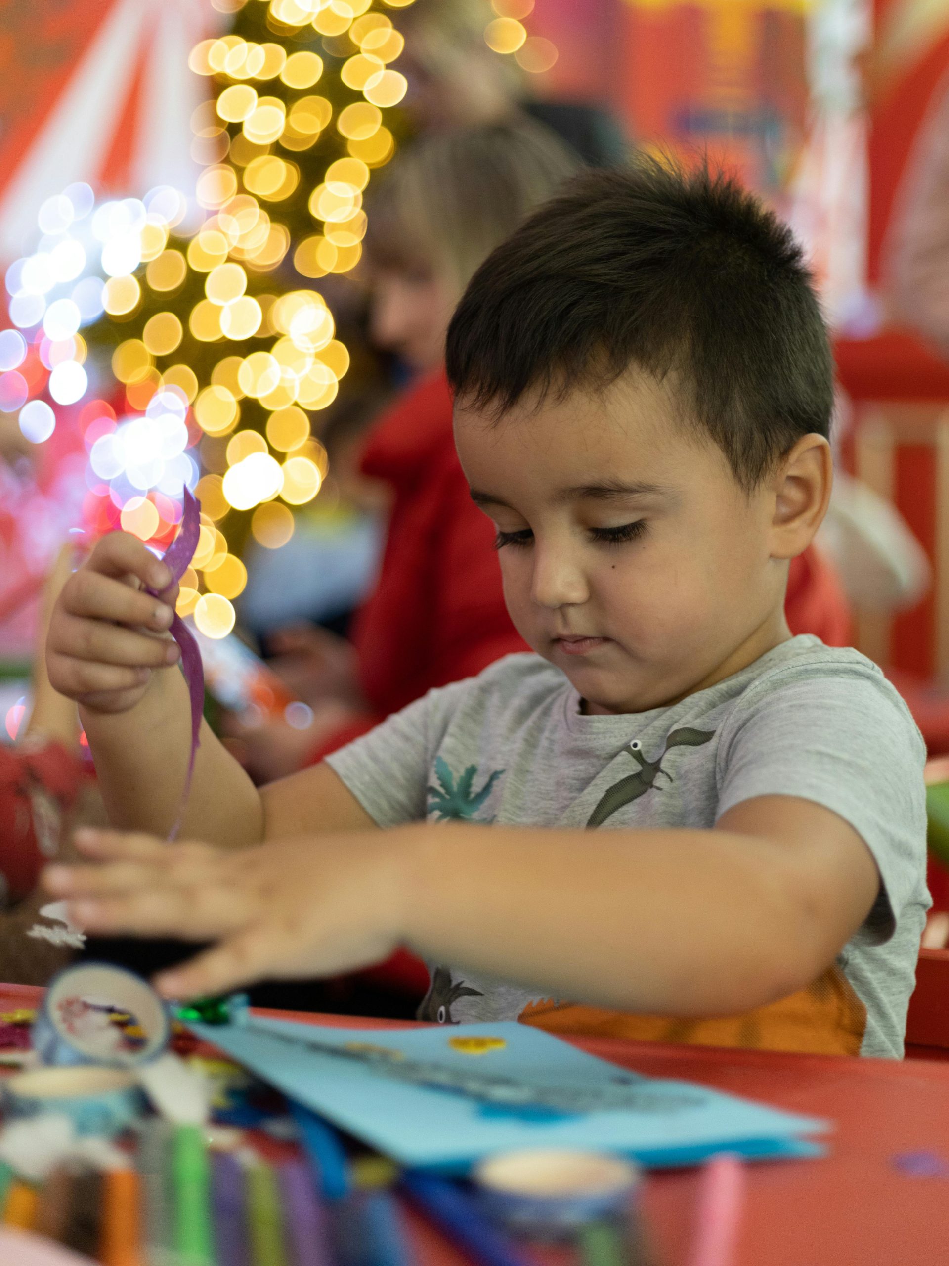 Young boy engaging in Christmas crafts with bokeh lights in the background. Un jeune garçon s'engageant dans des activités artisanales de Noël avec des lumières bokeh en arrière-plan.