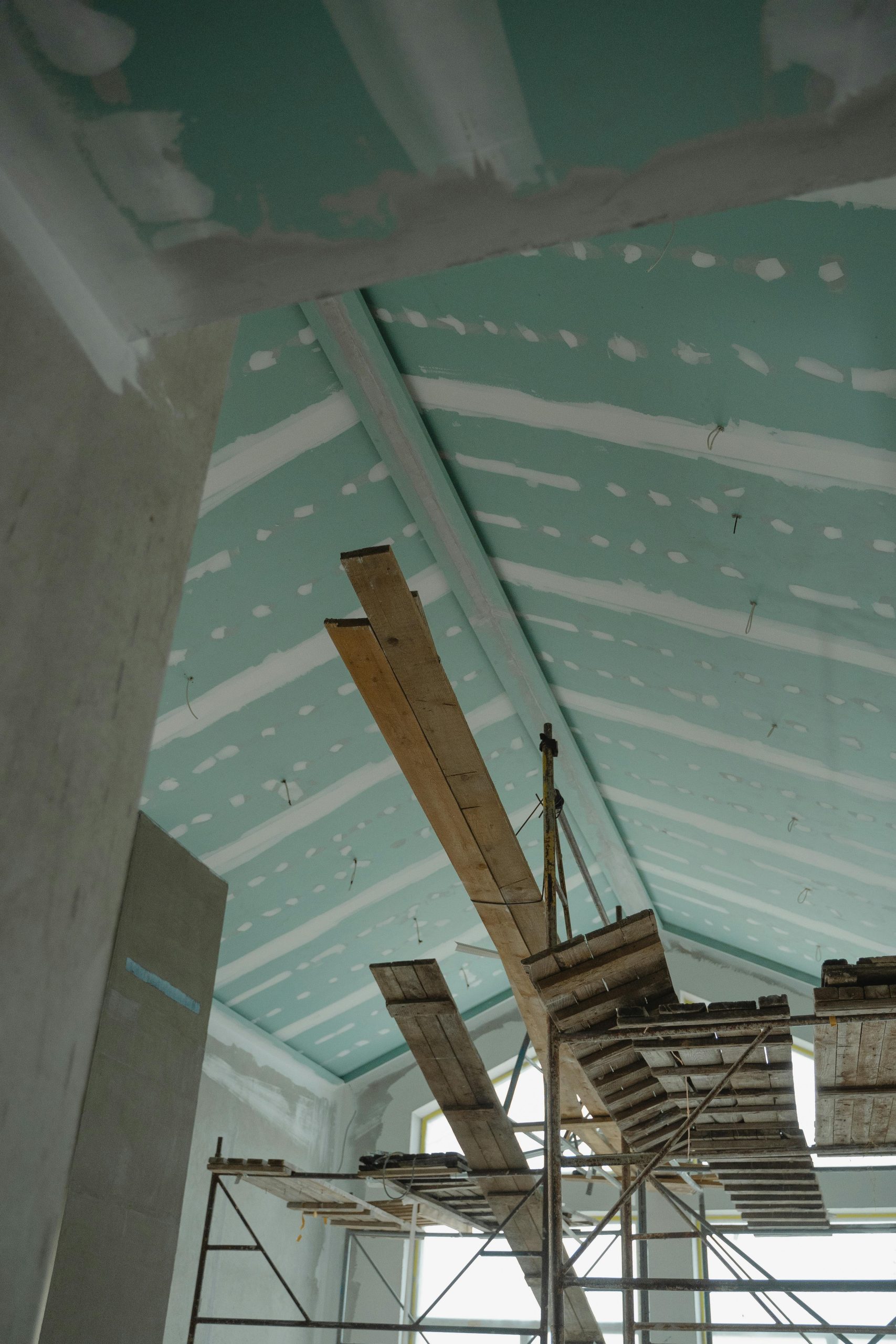 Scaffolding setup in an interior construction space with suspended ceiling boards and wooden planks. Configuration d'échafaudage dans un espace de construction intérieur avec des panneaux de plafond suspendus et des planches en bois.