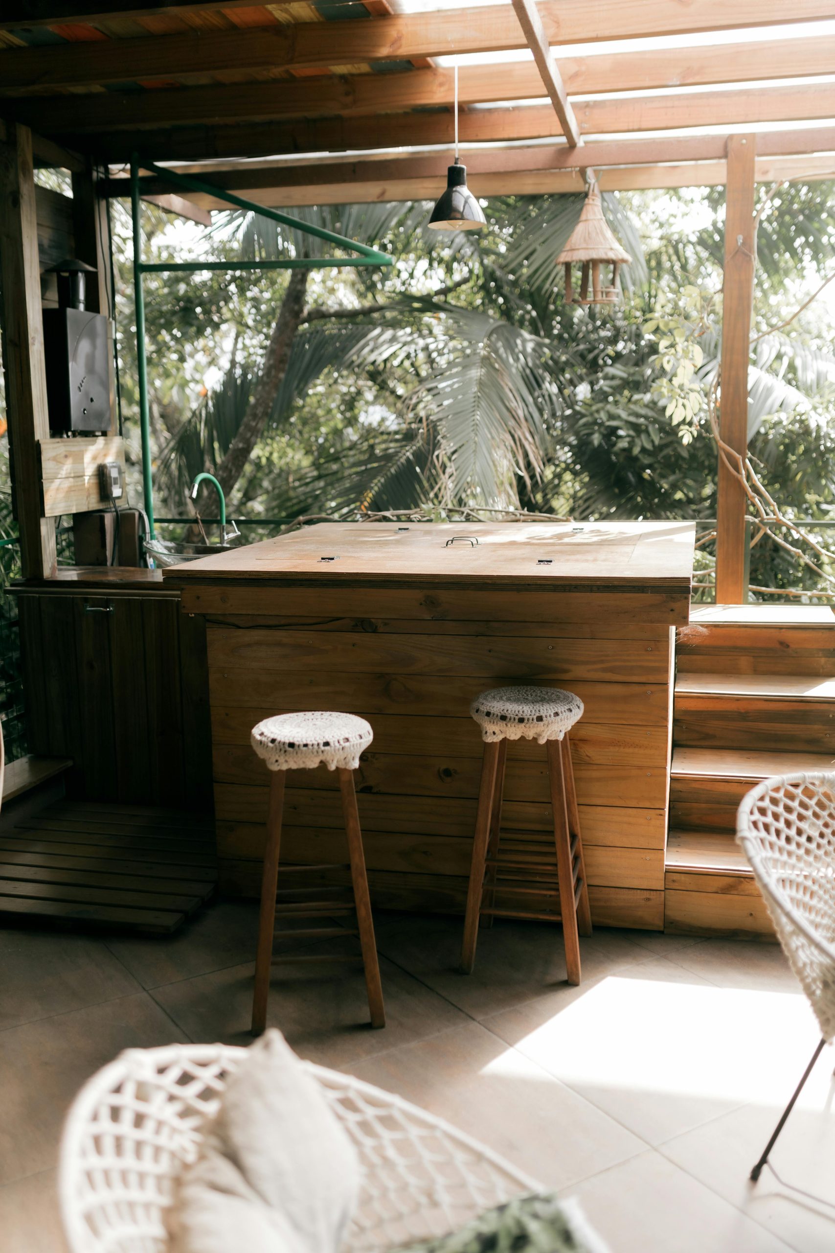 Charming outdoor bar with wooden stools and lush greenery, perfect for relaxation. Bar extérieur charmant avec des tabourets en bois et une verdure luxuriante, parfait pour la détente.