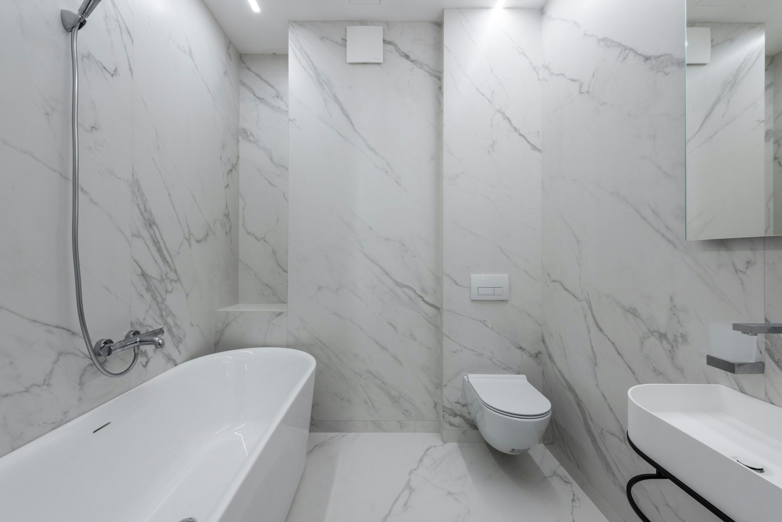 Interior of stylish bathroom with marble walls and bath placed near toilet and ceramic sink in light room with mirror Intérieur d'une salle de bain élégante avec des murs en marbre et une baignoire placée près des toilettes et d'un lavabo en céramique dans une pièce lumineuse avec miroir