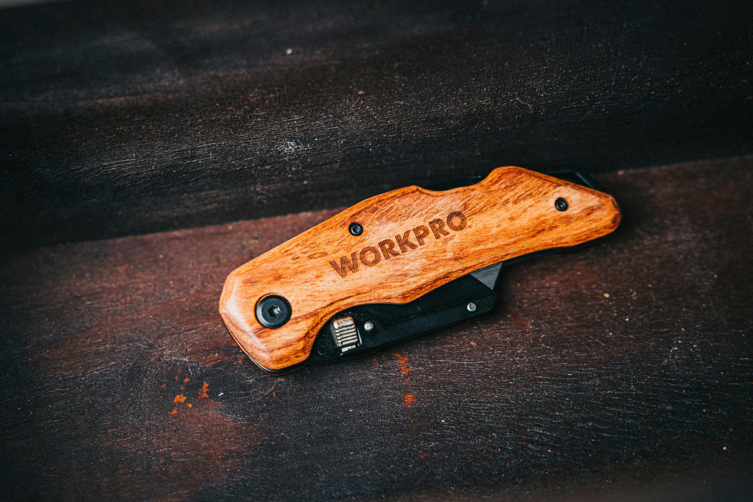 Close-up of a Workpro folding knife with wooden handle, perfect for camping and outdoor use. Gros plan d'un couteau pliant Workpro avec manche en bois, parfait pour le camping et les activités de plein air.