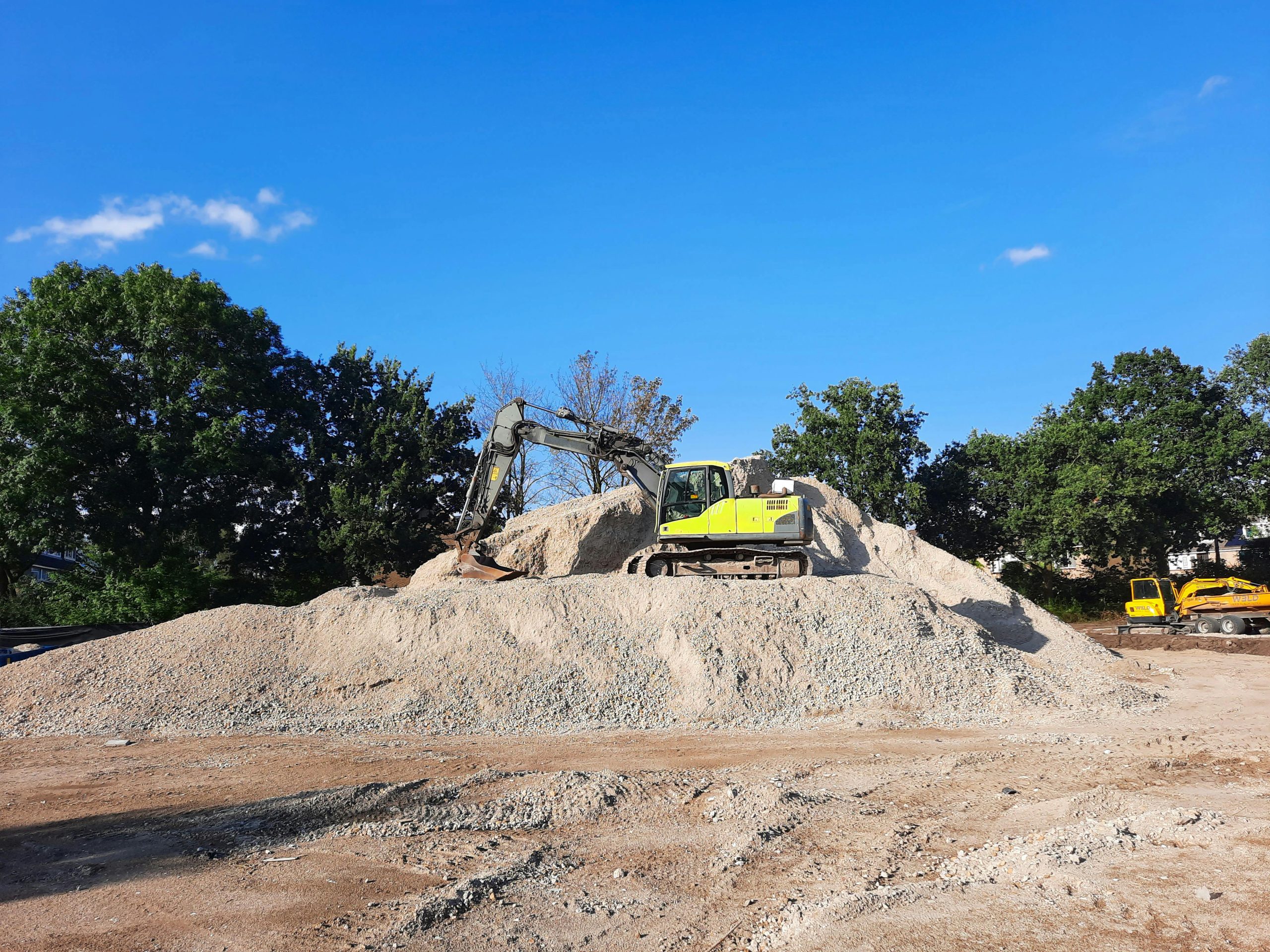 Excavator working on a gravel pile at an outdoor construction site with clear blue sky. Une pelle mécanique travaillant sur un tas de gravier sur un chantier de construction extérieur avec un ciel bleu clair.