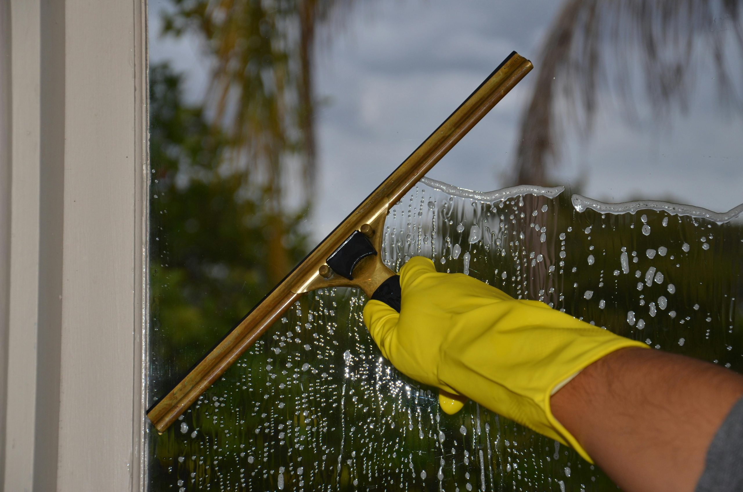Close-up of hand cleaning window with squeegee outdoors using yellow gloves. Gros plan d'une main nettoyant une fenêtre avec une raclette à l'extérieur avec des gants jaunes.