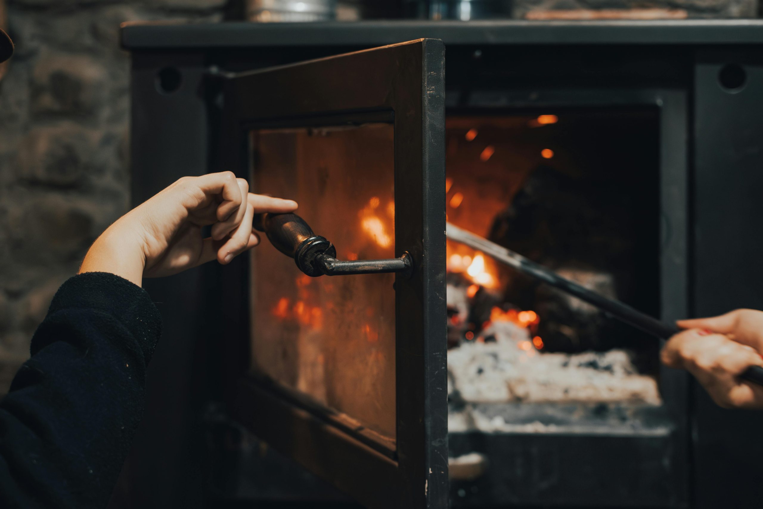 Hands tending to a warm, burning fireplace indoors, capturing the essence of comfort. Des mains s'occupant d'une cheminée chaude et brûlante à l'intérieur, capturant l'essence du confort.