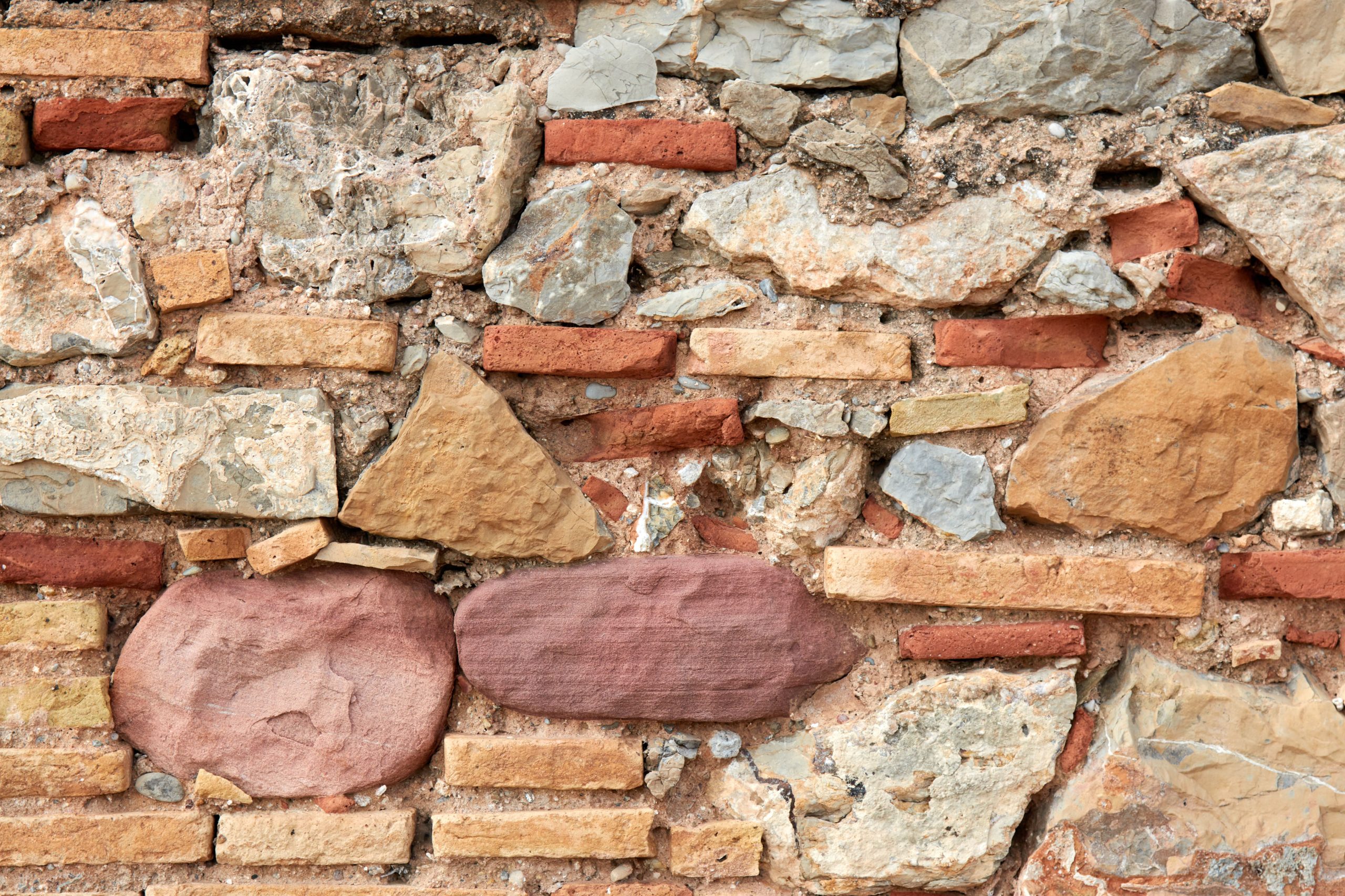 Detailed view of a rough textured stone and brick masonry wall, ideal for backgrounds. Vue détaillée d'un mur de maçonnerie en pierre et brique à texture rugueuse, idéal pour les arrière-plans.